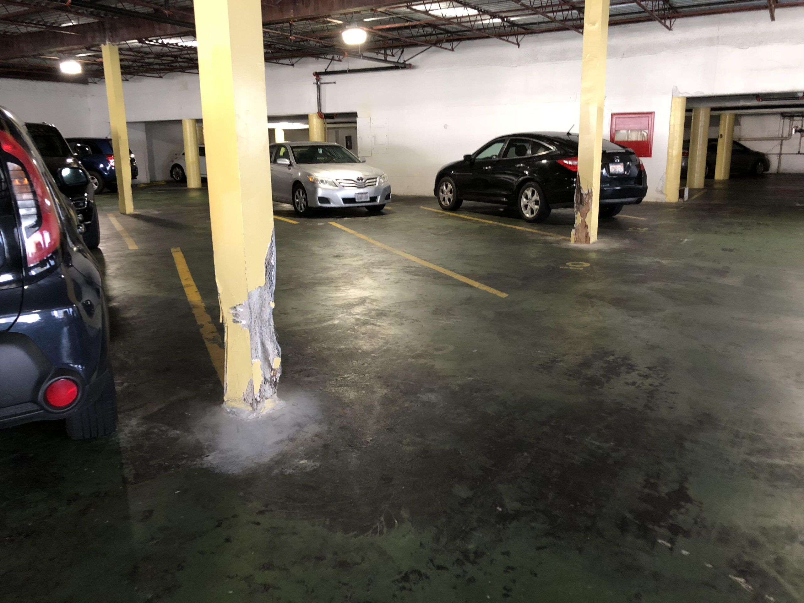 A damaged column in a parking garage that looks to have been hit by cars