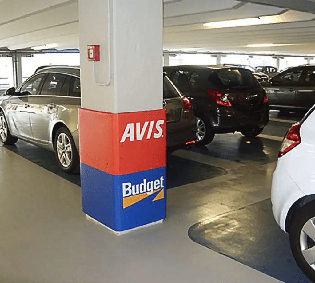 A column in a parking garage with a Cingo Protective Wrap installed that directs cars and pedestrians to Budget and Avis car rentals