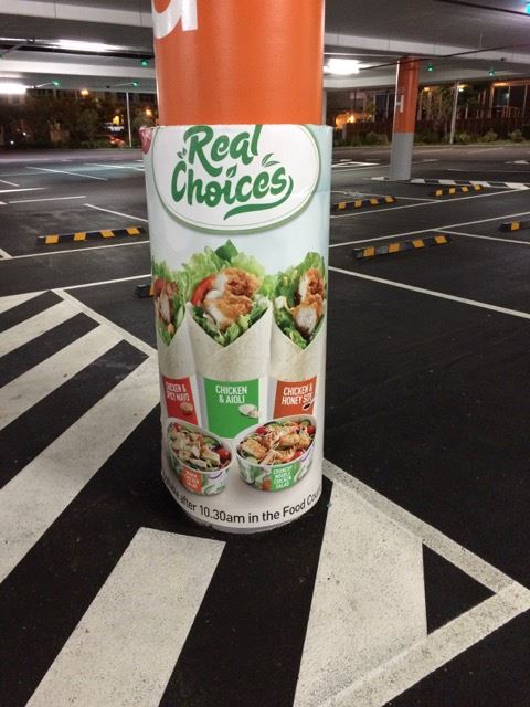 A round column in a parking garage protected by a Cingo Protective Wrap that advertises a food brand