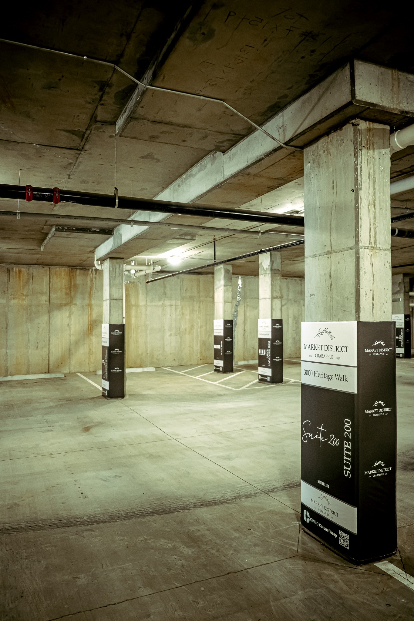 Six columns in a parking garage with branded Cingo Protective Wraps, each advertising a different shop in the building.