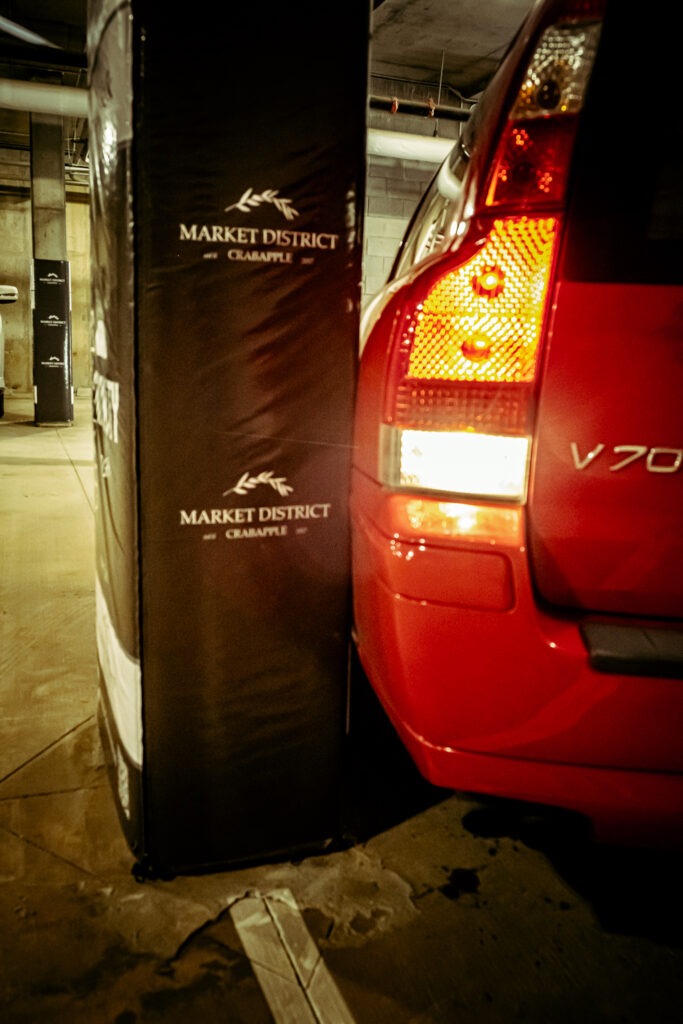 A red car backing up into a column in a parking lot, but protected from damaging the column or the car with a Cingo Protective Wrap