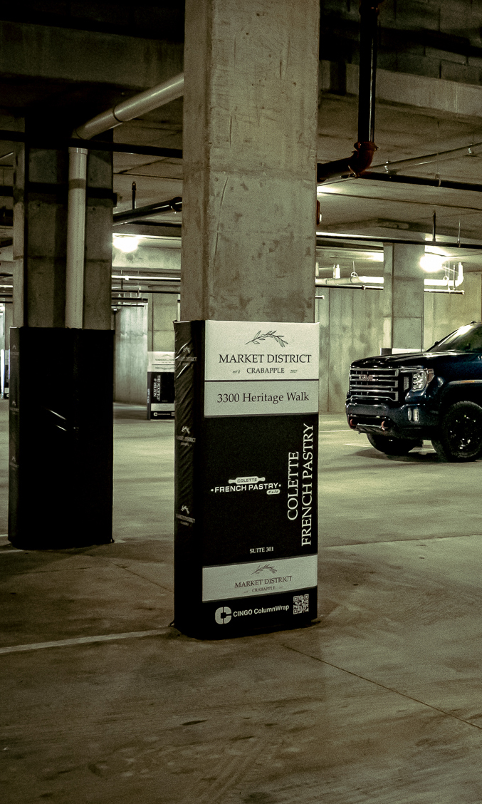 A branded Cingo Protective Wrap installed on a concrete pillar in a parking lot, advertising a French pastry shop in the building